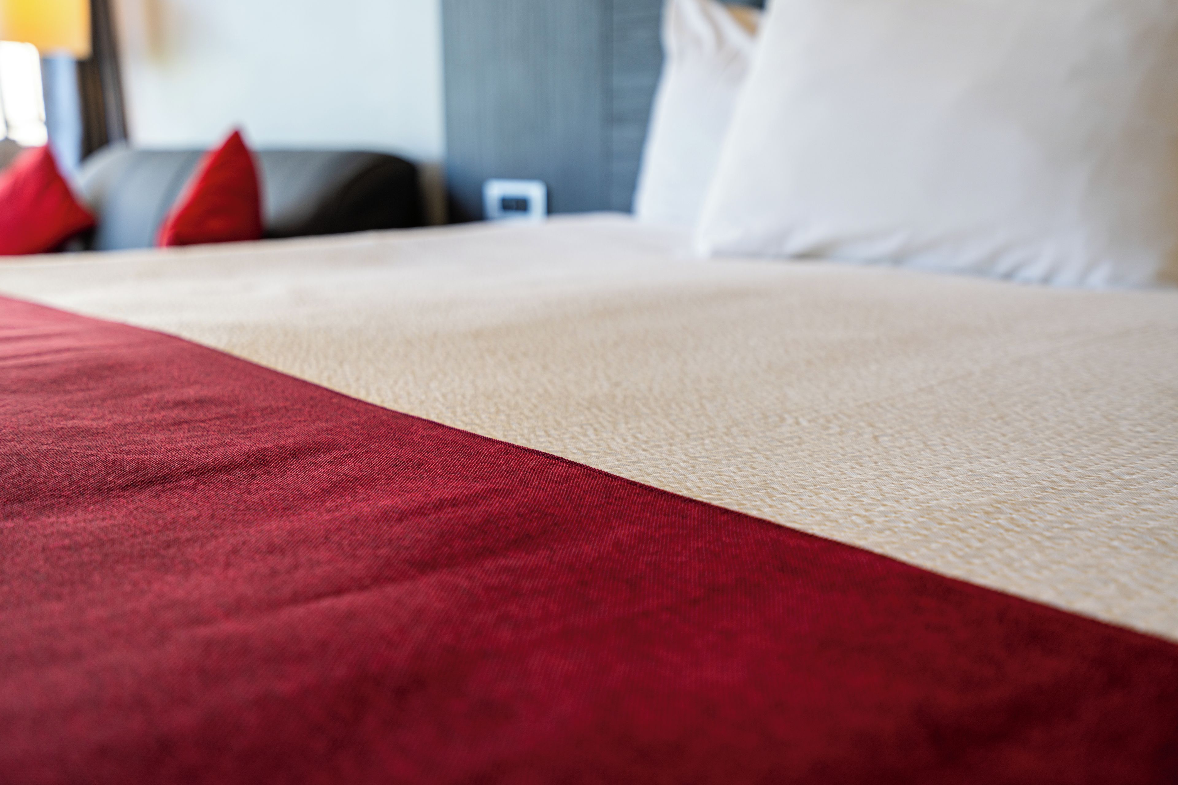 A bed with a red and beige bedspread, a white pillow, and a red pillow.