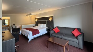 A hotel room with a bed, a sofa, a desk, and a chair. - Rodeway Inn King William (Huntsville)
