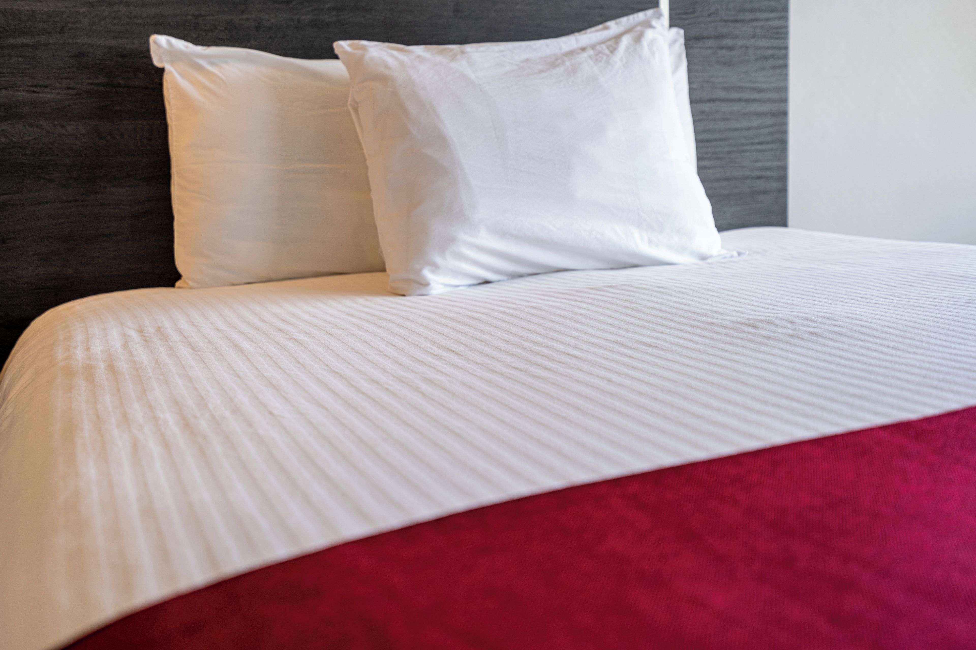 Un lit avec une literie blanche et un élément décoratif rouge.