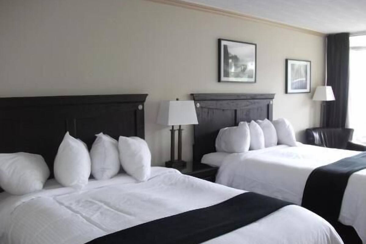 Habitación de hotel con dos camas, una mesita de noche con lámpara y una silla.