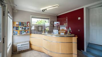 A reception desk with a wooden counter, a window with a view of greenery, a wall-mounted clock, and a sign indicating no cash accepted.