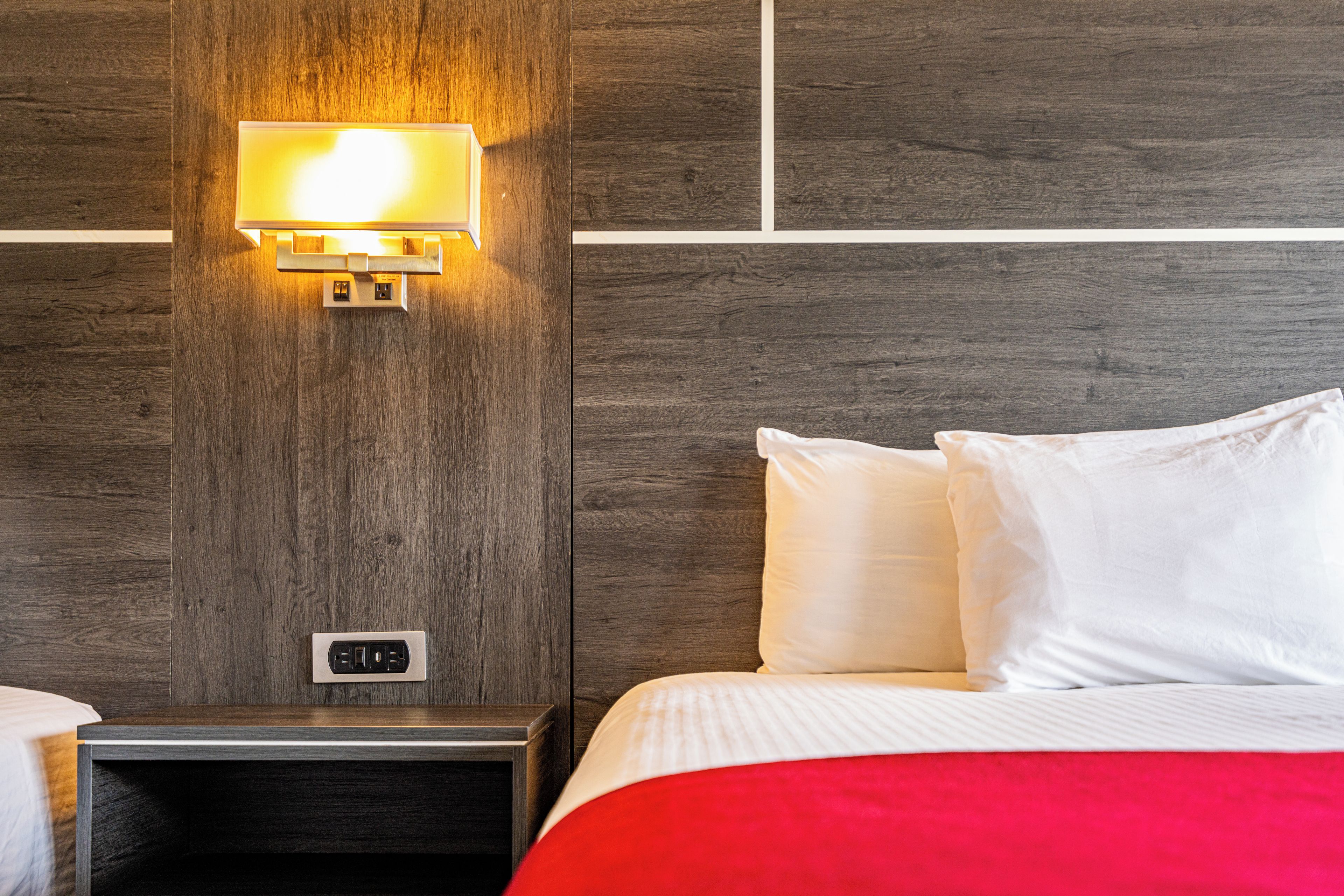 A hotel room with a wooden headboard, a bedside table, a lamp, and a bed with white bedding.