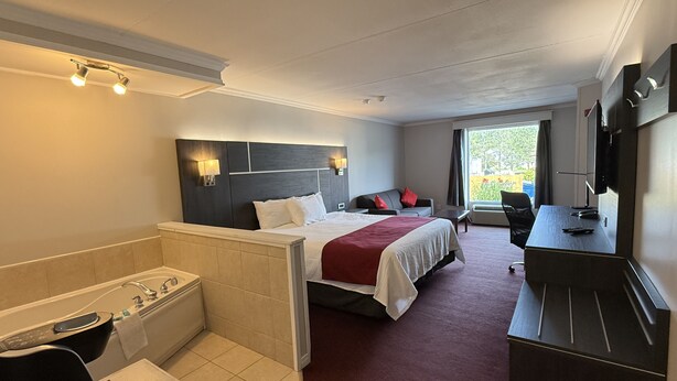 A hotel room with a bed, a desk, a chair, a TV, and a window. - Rodeway Inn King William (Huntsville)