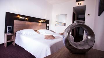 Hotellihuone, jossa on sänky, yöpöytä, peili ja koristeellinen maljakko.