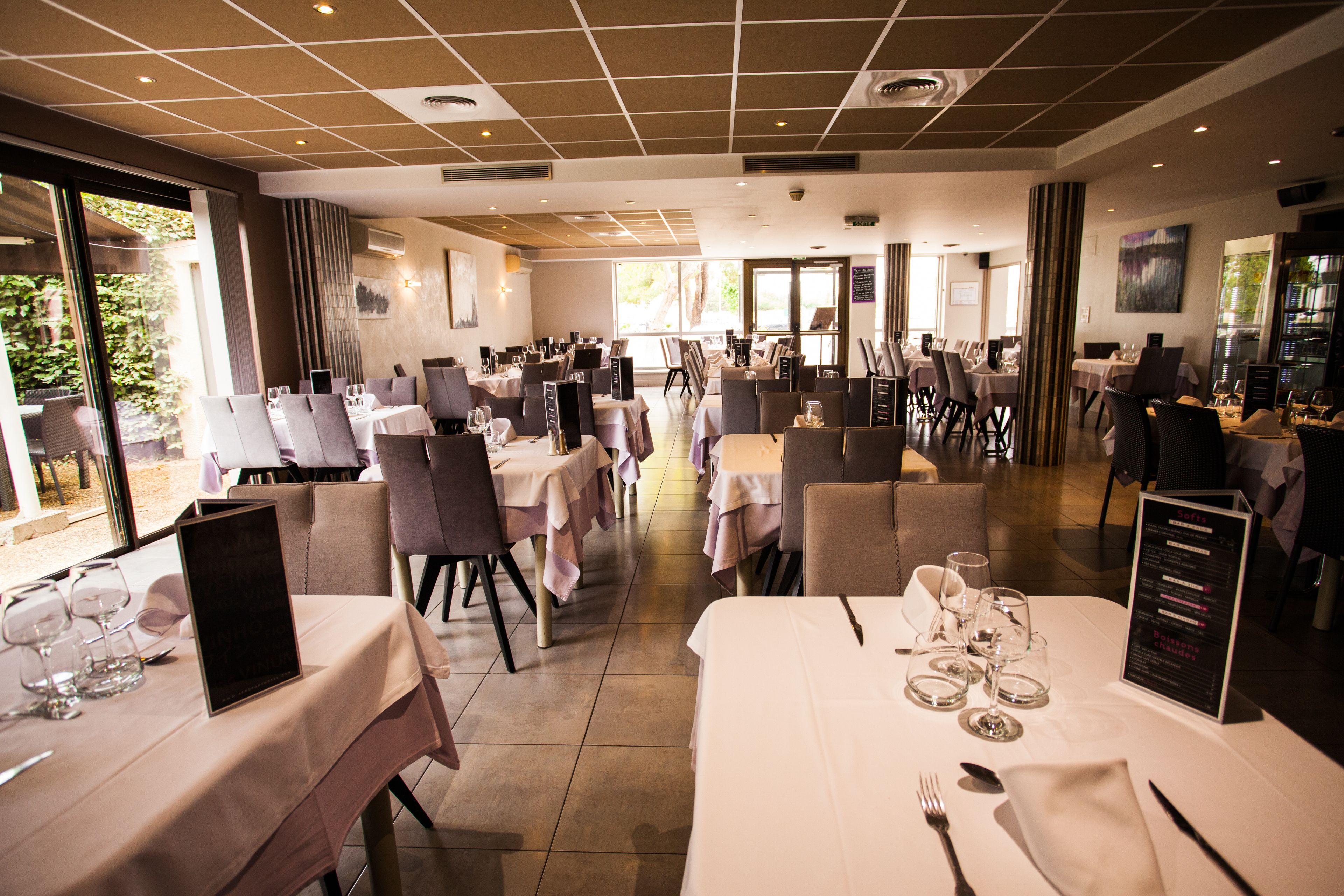 A spacious dining area with multiple tables set for service, large windows providing natural light, and a modern interior design.