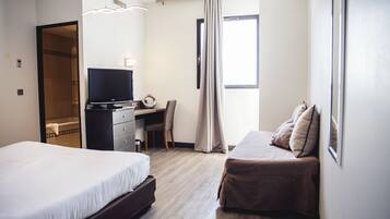 A hotel room with a bed, a desk, a chair, a television, and a window with curtains.