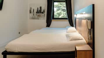 Een slaapkamer met een bed, nachtkastje, gordijnen voor het raam en een telefoon aan de muur.