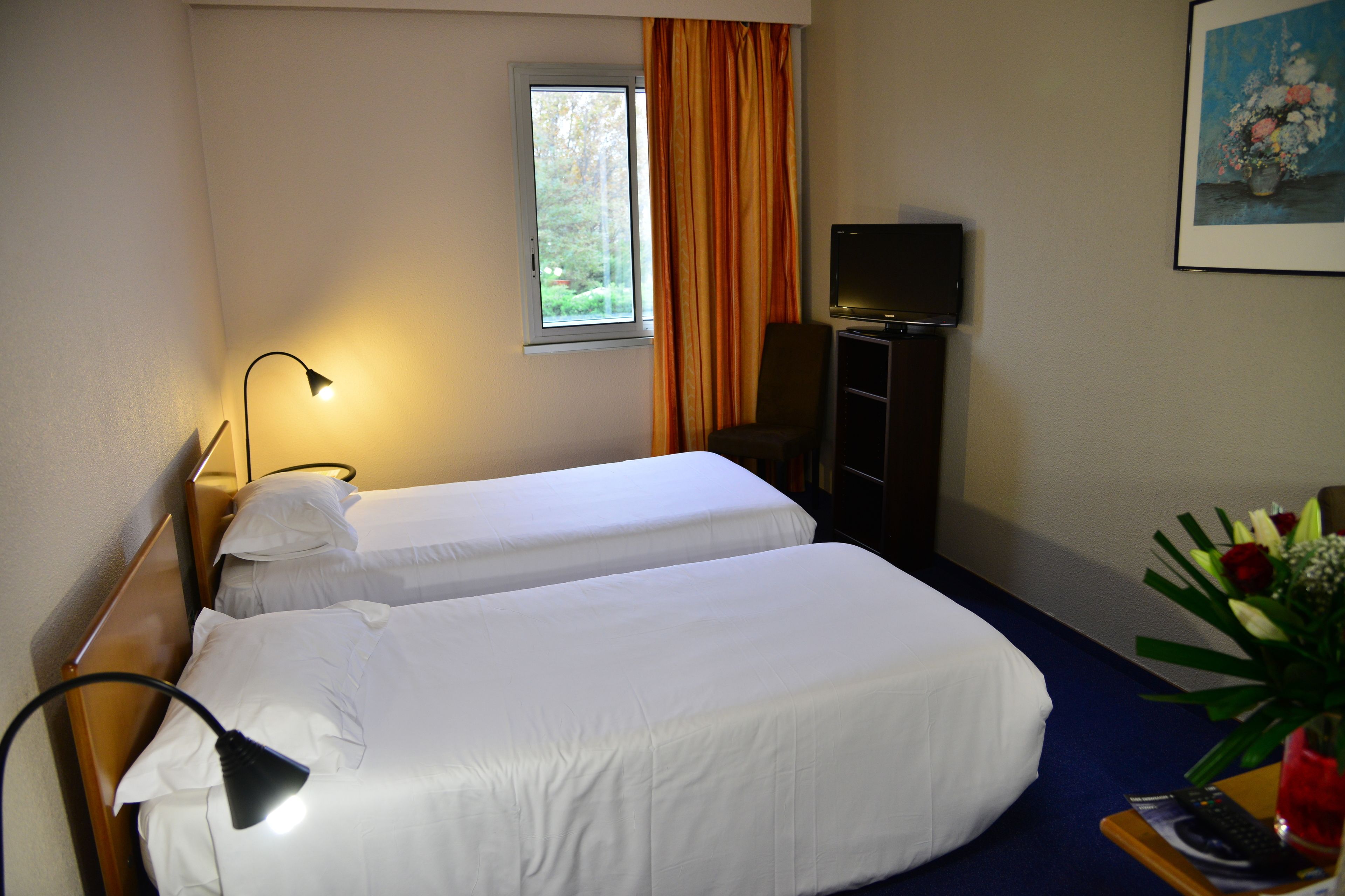 Habitación de hotel con dos camas, televisor, escritorio y ventana con cortinas.