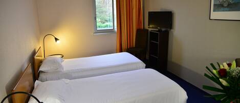 A hotel room with two beds, a television, a desk, and a window with curtains.