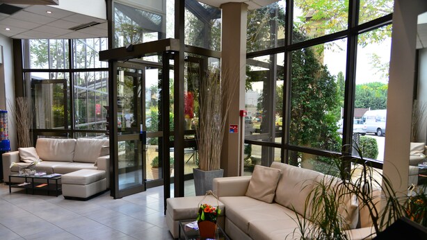 A spacious lobby with a beige sofa, a coffee table, and a potted plant. - Aéroport Hôtel (Mauguio)