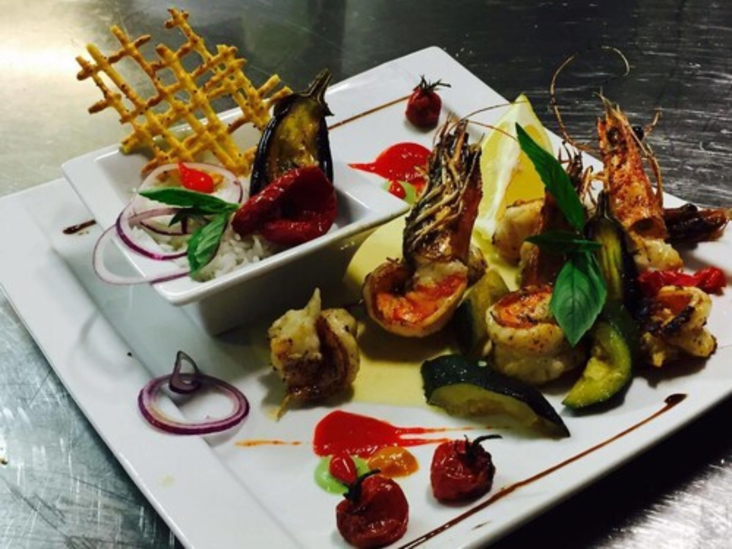 A plate of food with various dishes including grilled shrimp, vegetables, and a waffle.