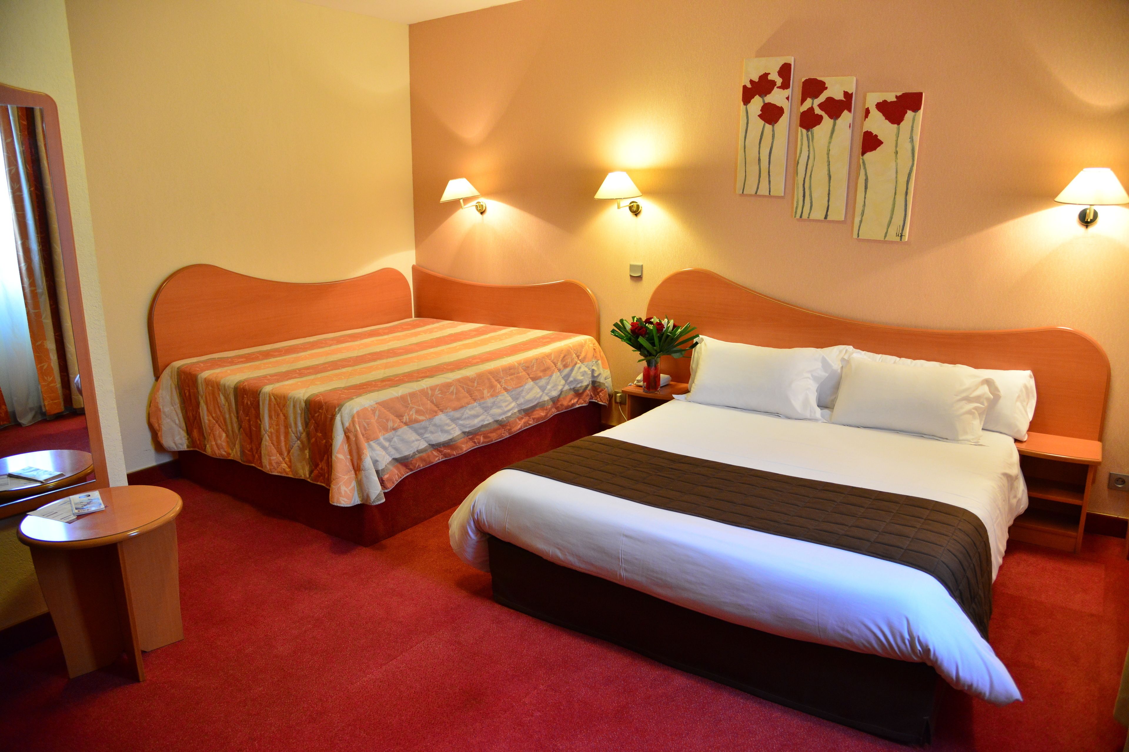 A hotel room with two beds, a small round table, and a nightstand with a lamp.
