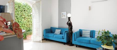 A living room with two blue sofas, a floor lamp, a potted plant, and a white air conditioner on the wall.