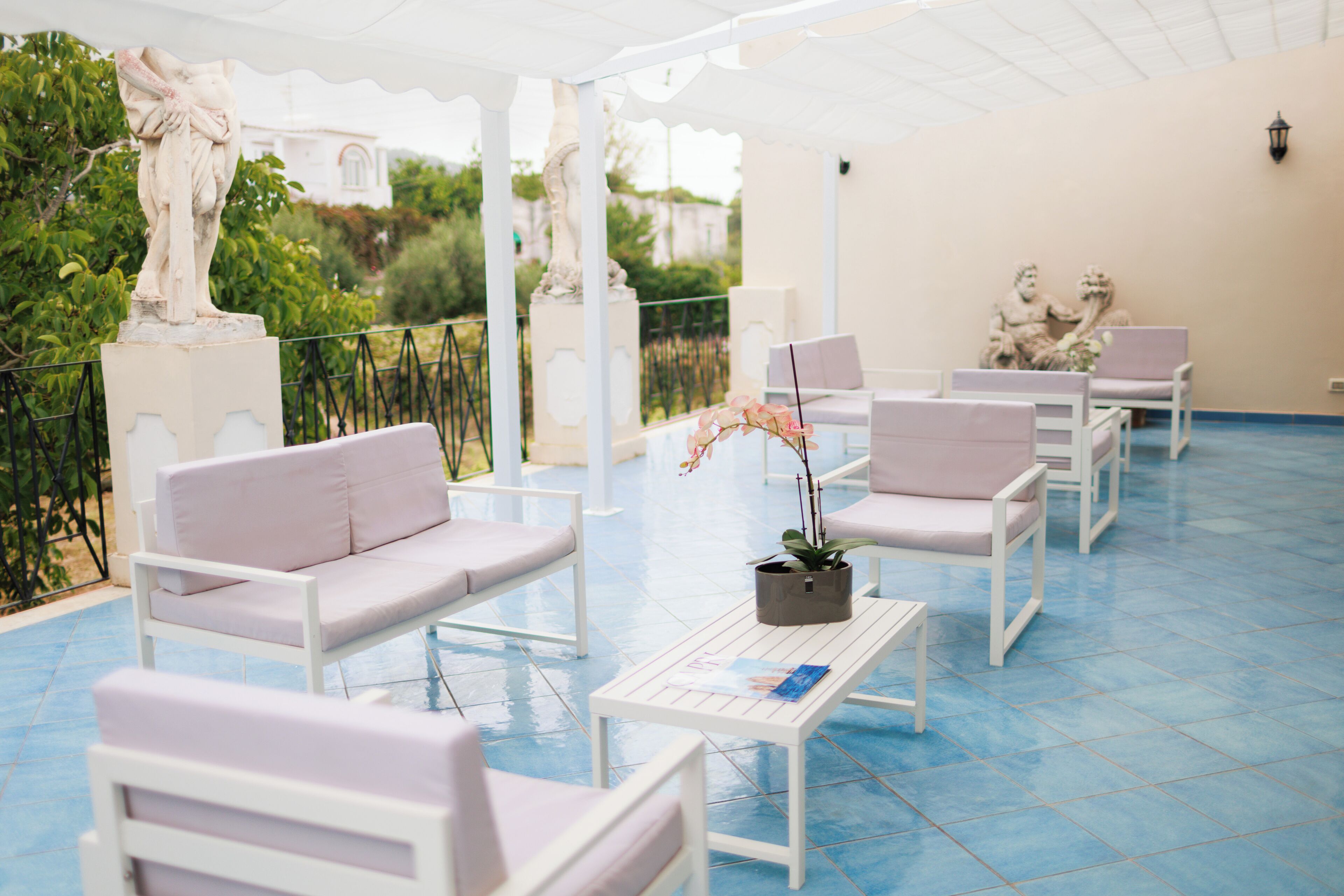 Un espace extérieur aménagé avec des meubles blancs, une table sur laquelle est posé un magazine et des statues décoratives.