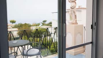 Een balkon met een tafel en stoelen, een standbeeld en uitzicht op zee en gebouwen.