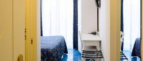 A hotel room with a bed, a desk, a chair, and a mirror.