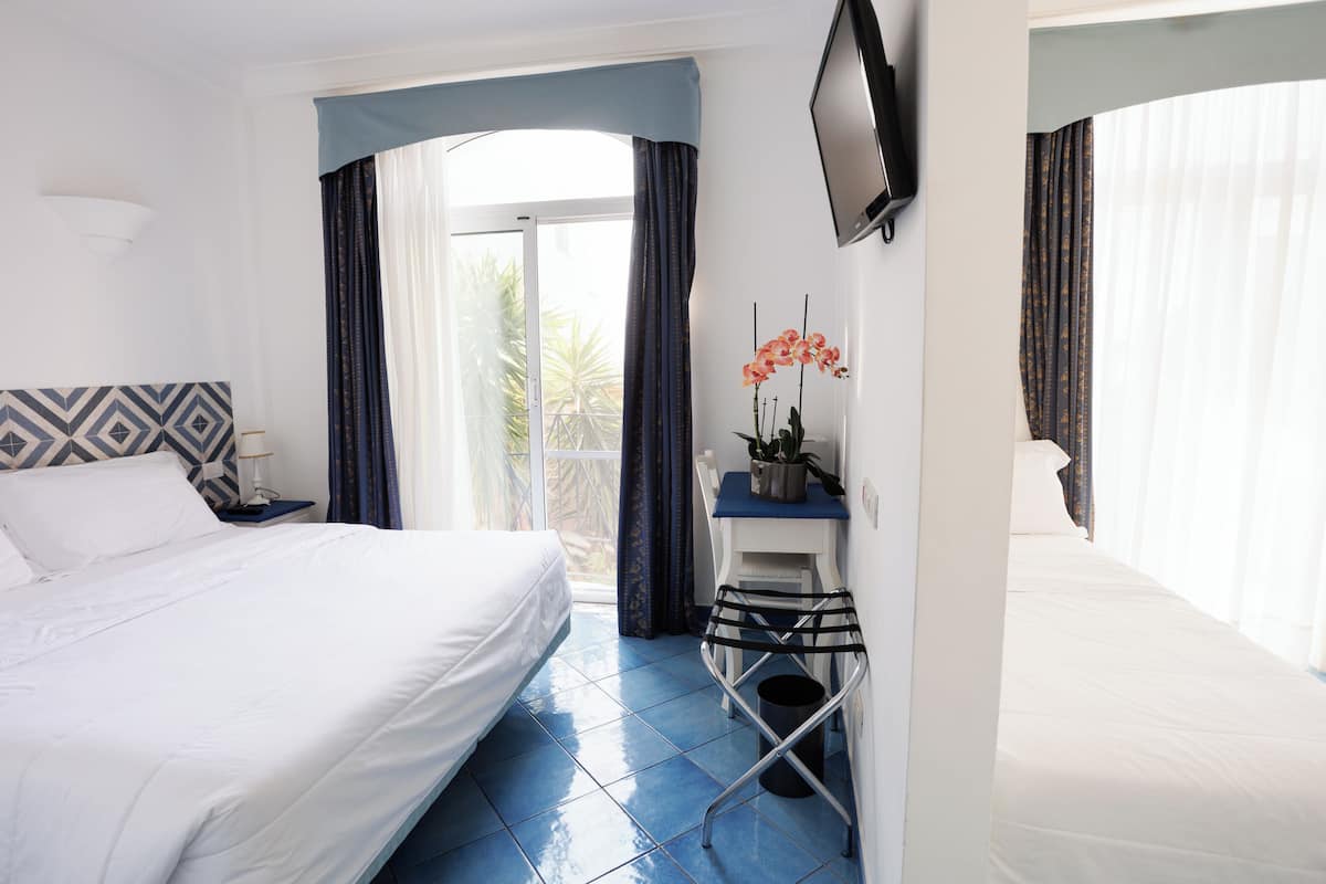 Ein Hotelzimmer mit einem Bett, einem Schreibtisch mit Stuhl, einem Fernseher und einem Fenster mit Vorhängen.