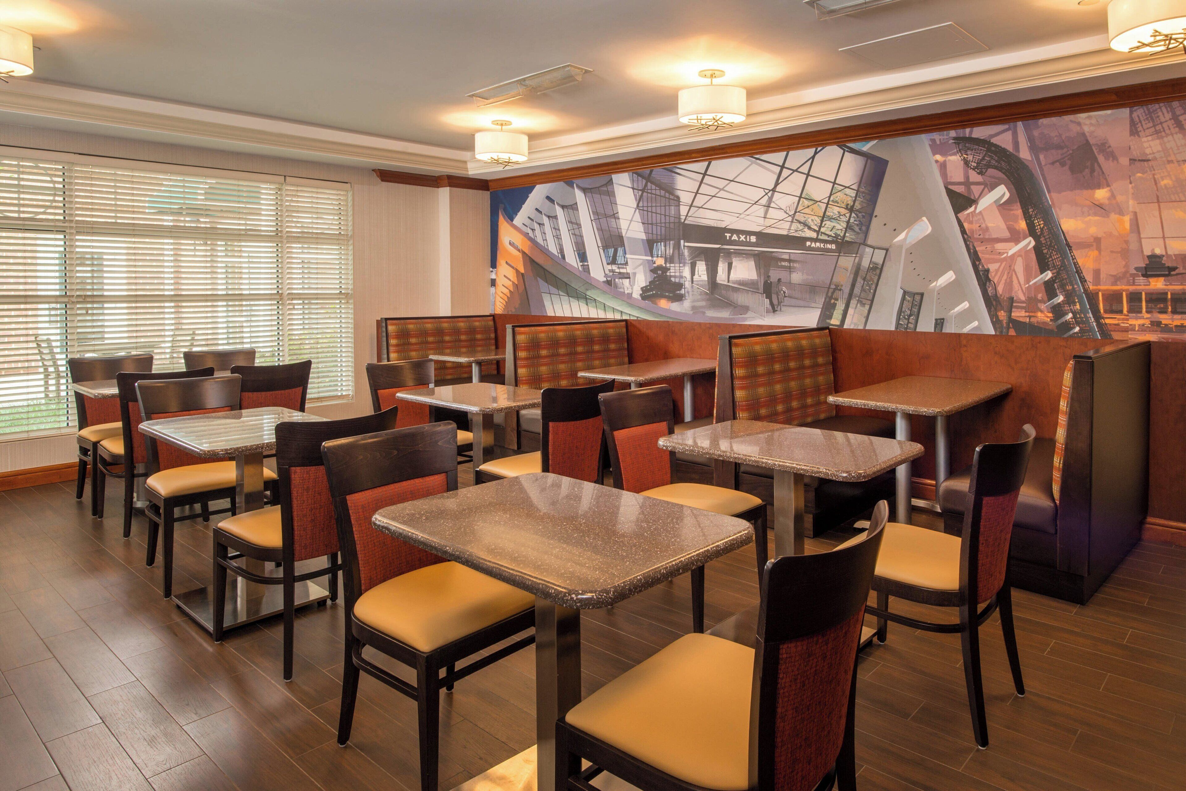 Een restaurant met zitjes en tafels, houten vloeren en een muurschildering van een stadsgezicht.