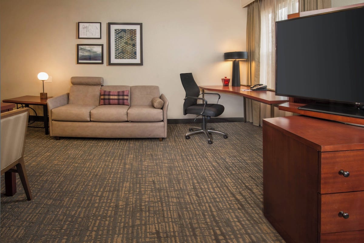 A hotel room with a sofa, a desk with a lamp, a television, and a chair.