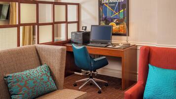 A hotel room with a wooden desk, a blue office chair, a brown sofa, and a red armchair.