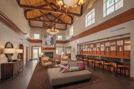 A spacious lobby with a high ceiling, wooden beams, a fireplace, a bar area, and comfortable seating.