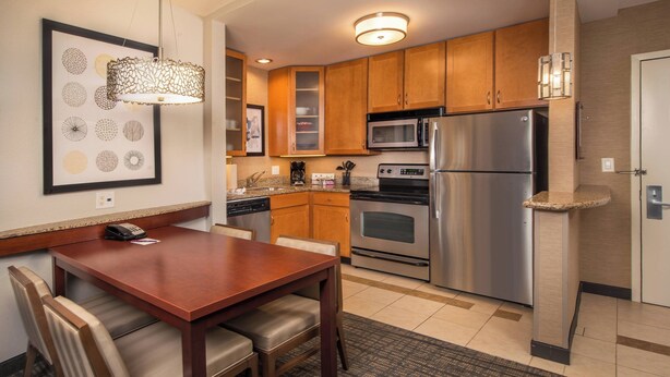 A modern kitchen with wooden cabinets, stainless steel appliances, and a dining area with a wooden table and chairs. - Residence Inn by Marriott Dulles Airport At Dulles 28 Centre (Sterling)