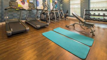 A gym with treadmills, elliptical machines, a bench, and dumbbells.