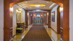 Un hall de hotel con suelo de mármol, columnas de madera, una mesa de recepción e iluminación en las paredes.