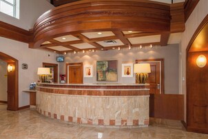 A hotel reception area with a curved marble counter, wooden ceiling beams, and framed artwork on the walls.