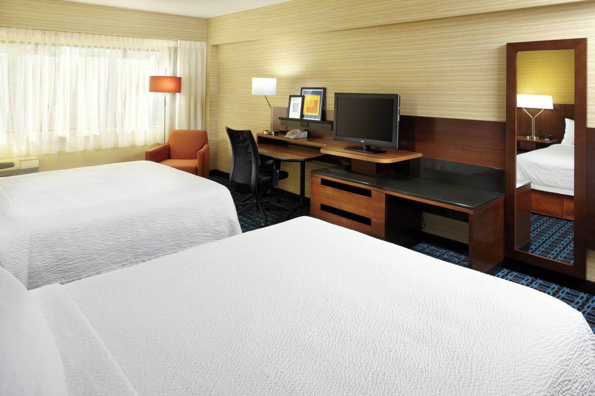 Ein Hotelzimmer mit zwei Betten, einem Schreibtisch mit Fernseher, einem Sessel und einem Spiegel.