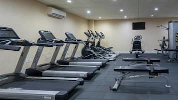 Une salle de sport équipée de plusieurs tapis de course, d’appareils de musculation et d’un téléviseur fixé au mur.