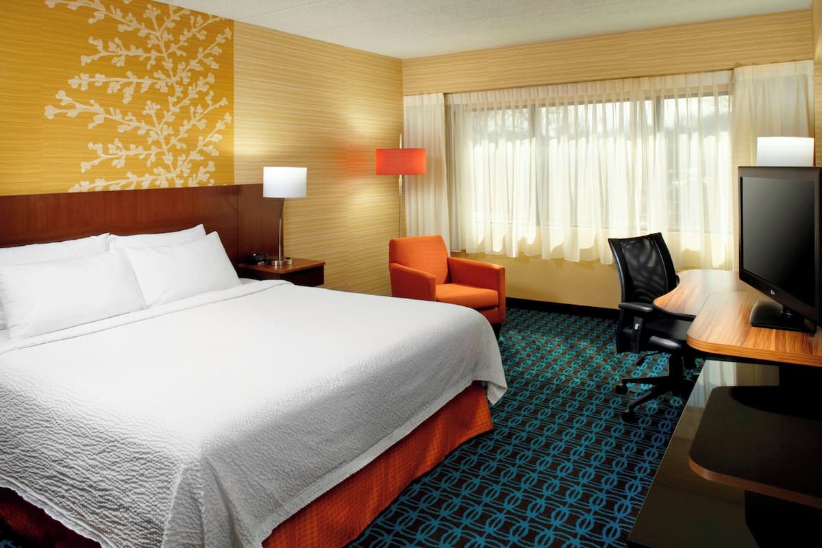 Ein Hotelzimmer mit einem großen Bett, einem orangefarbenen Sessel, einem Schreibtisch mit Computer und einem Fernseher.
