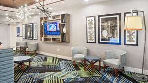 A hotel lobby with a modern design, featuring a large TV screen, comfortable seating, and a patterned carpet.