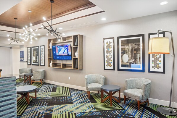 A hotel lobby with a modern design, featuring a large TV screen, comfortable seating, and a patterned carpet. - Holiday Inn Express & Suites Stroudsburg-Poconos by IHG (Stroudsburg)