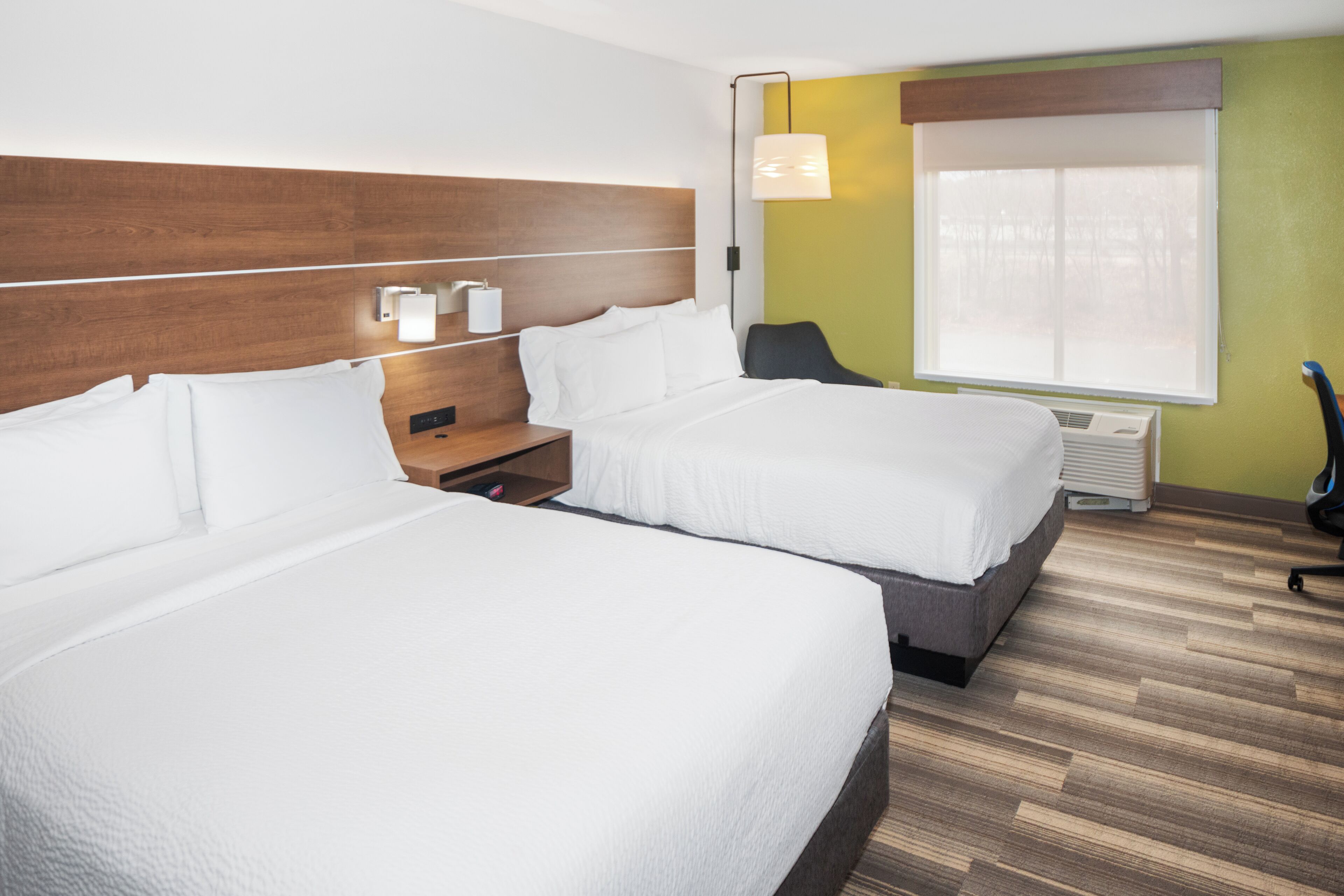 Habitación de hotel con dos camas, una mesita de noche, un escritorio, una silla y una ventana con persianas.