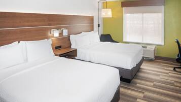 Habitación de hotel con dos camas, una mesita de noche, un escritorio, una silla y una ventana con persianas.