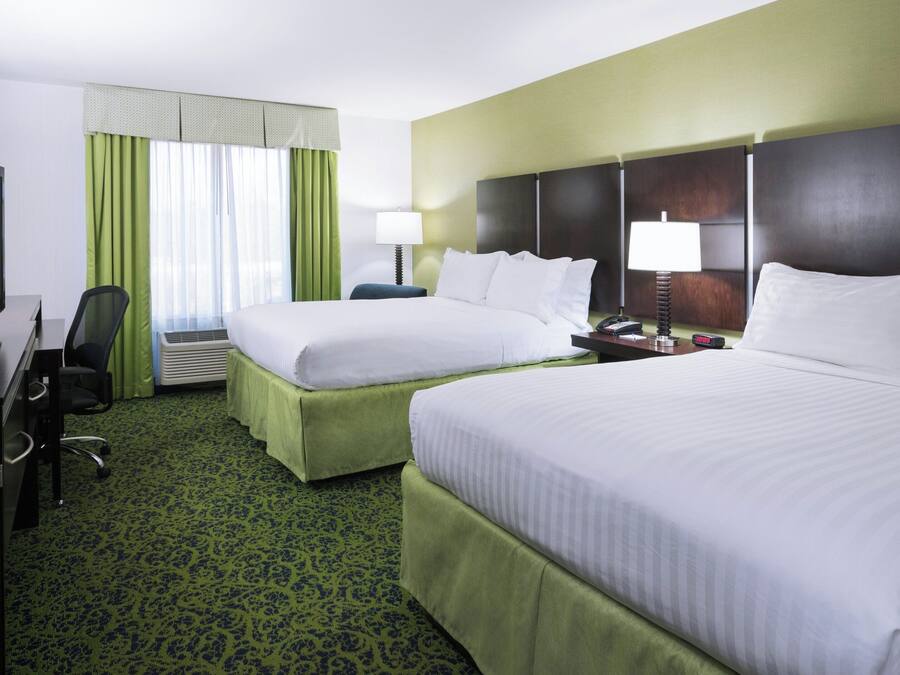 A hotel room with two beds, a desk with a television, a chair, and a lamp.