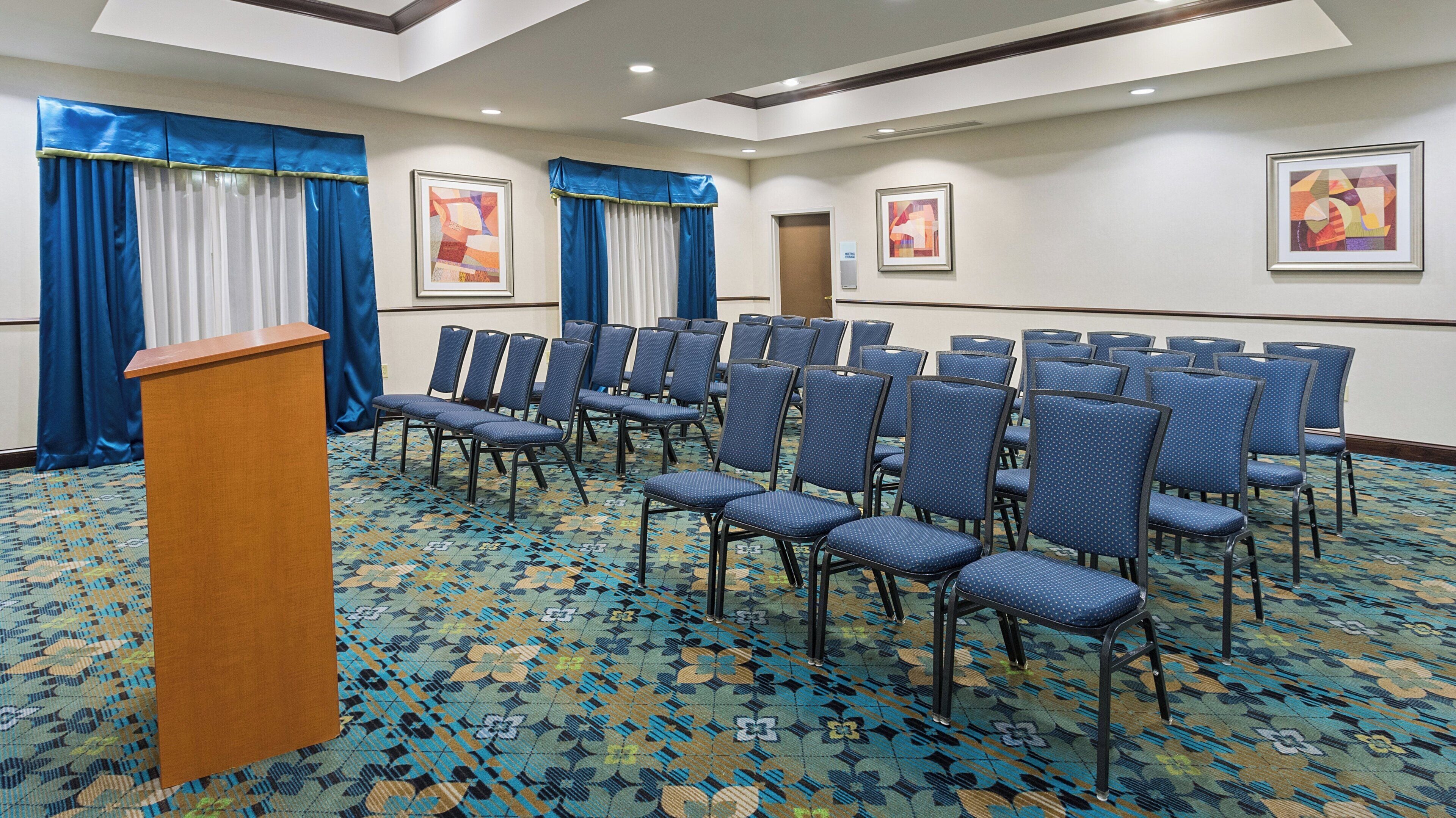 A conference room with rows of chairs, a podium, and two doors.