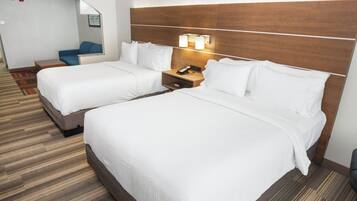 A hotel room with two beds, a nightstand with a phone, and a seating area with a chair and a small table.