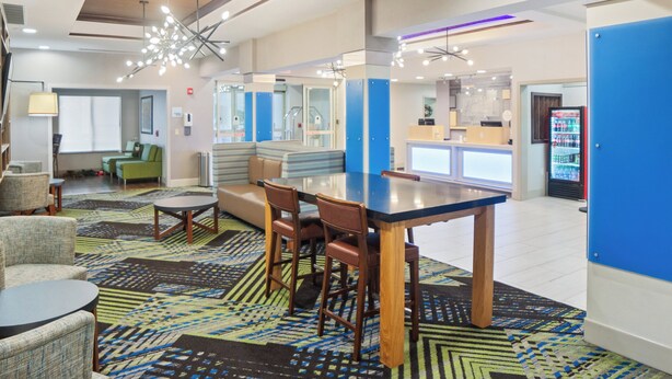 A modern hotel lobby with a central dining area, seating, and a reception desk.