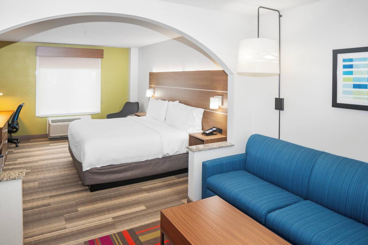 Une chambre d’hôtel avec un lit, un canapé bleu, un bureau et une lampe.