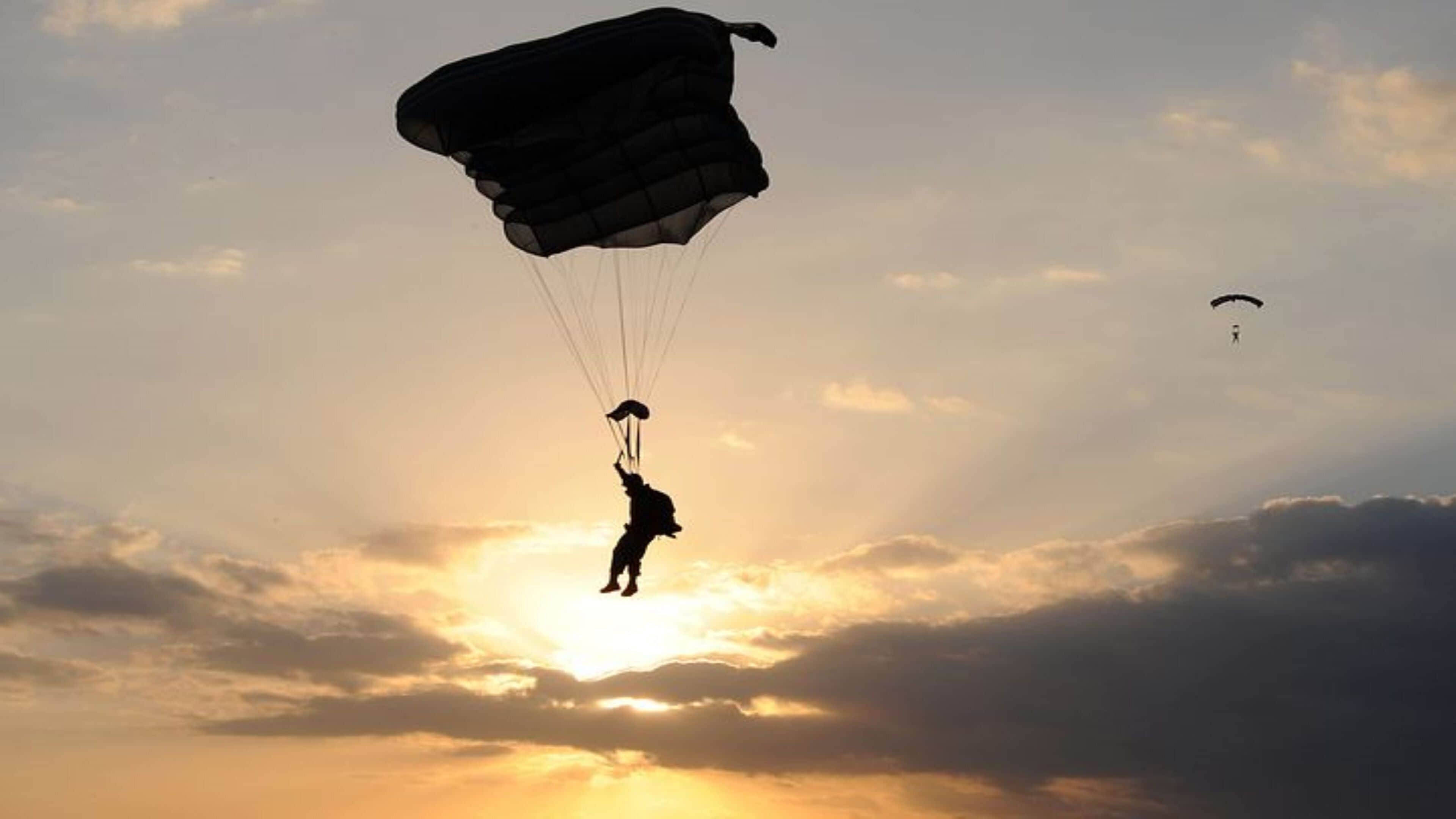 Eine Person mit Fallschirm springt in den Abendhimmel.