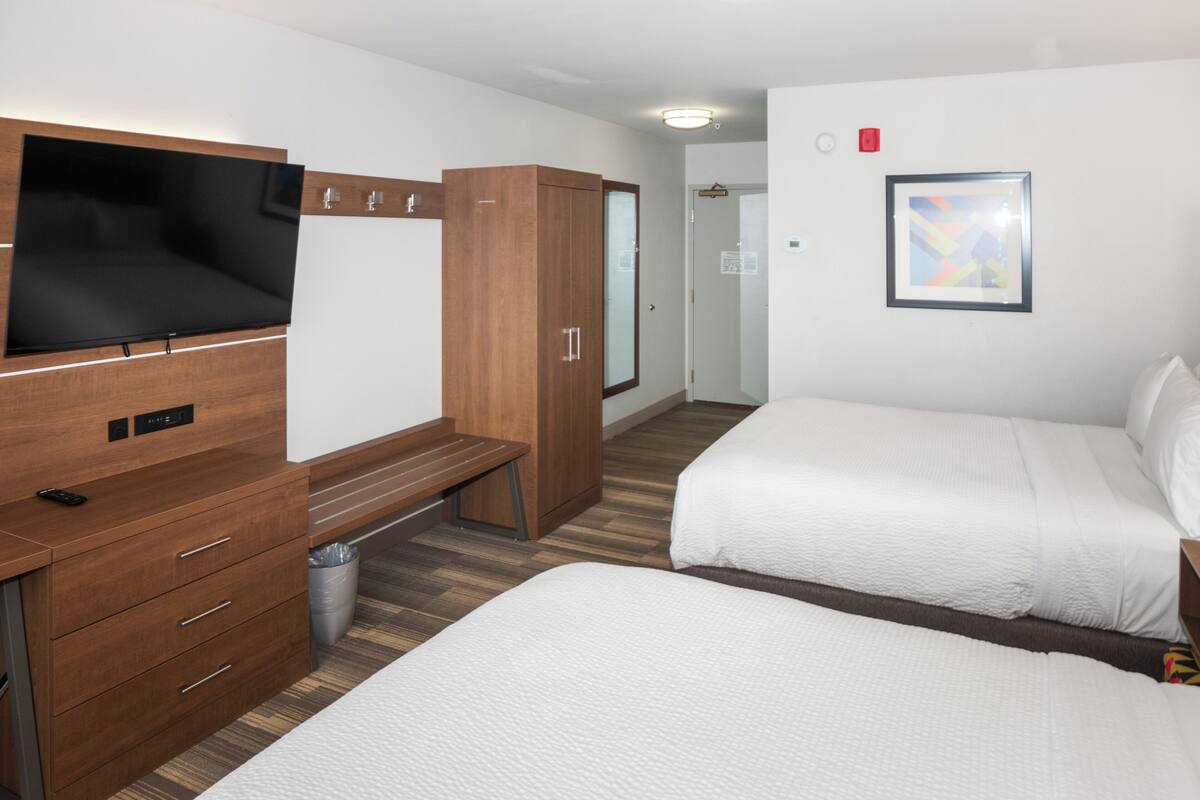 Une chambre d’hôtel avec un lit, un téléviseur fixé au mur, une armoire en bois et un banc.