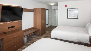 A hotel room with a bed, a TV mounted on the wall, a wooden wardrobe, and a bench.