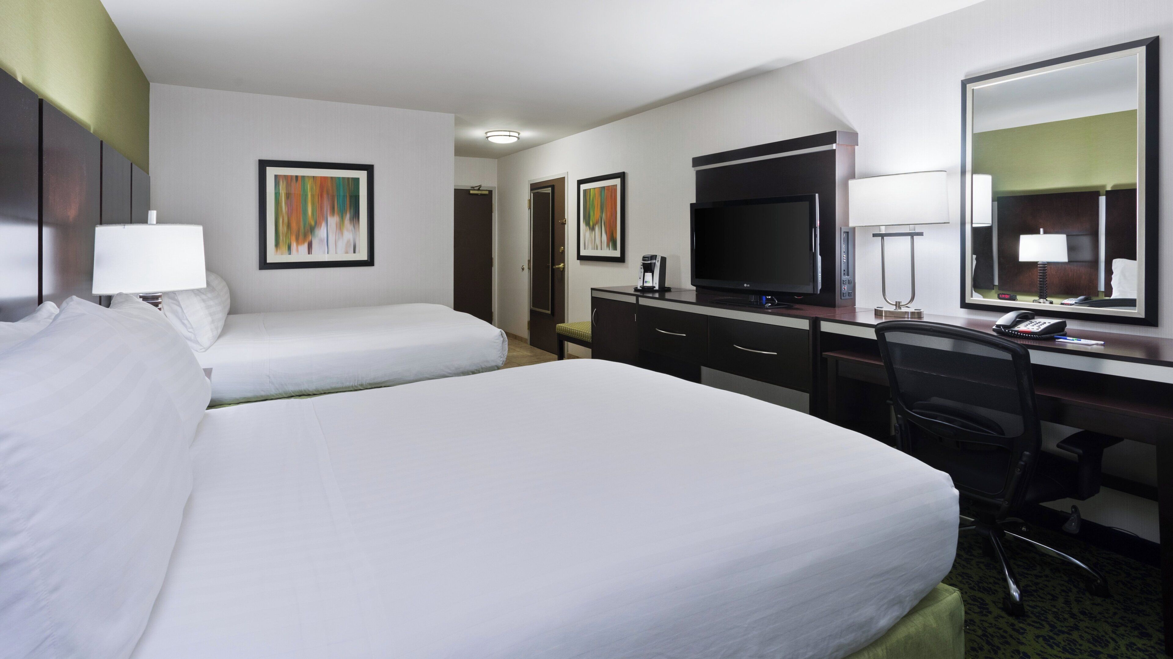 Quarto de hotel com duas camas, uma escrivaninha com computador, televisão e espelho.