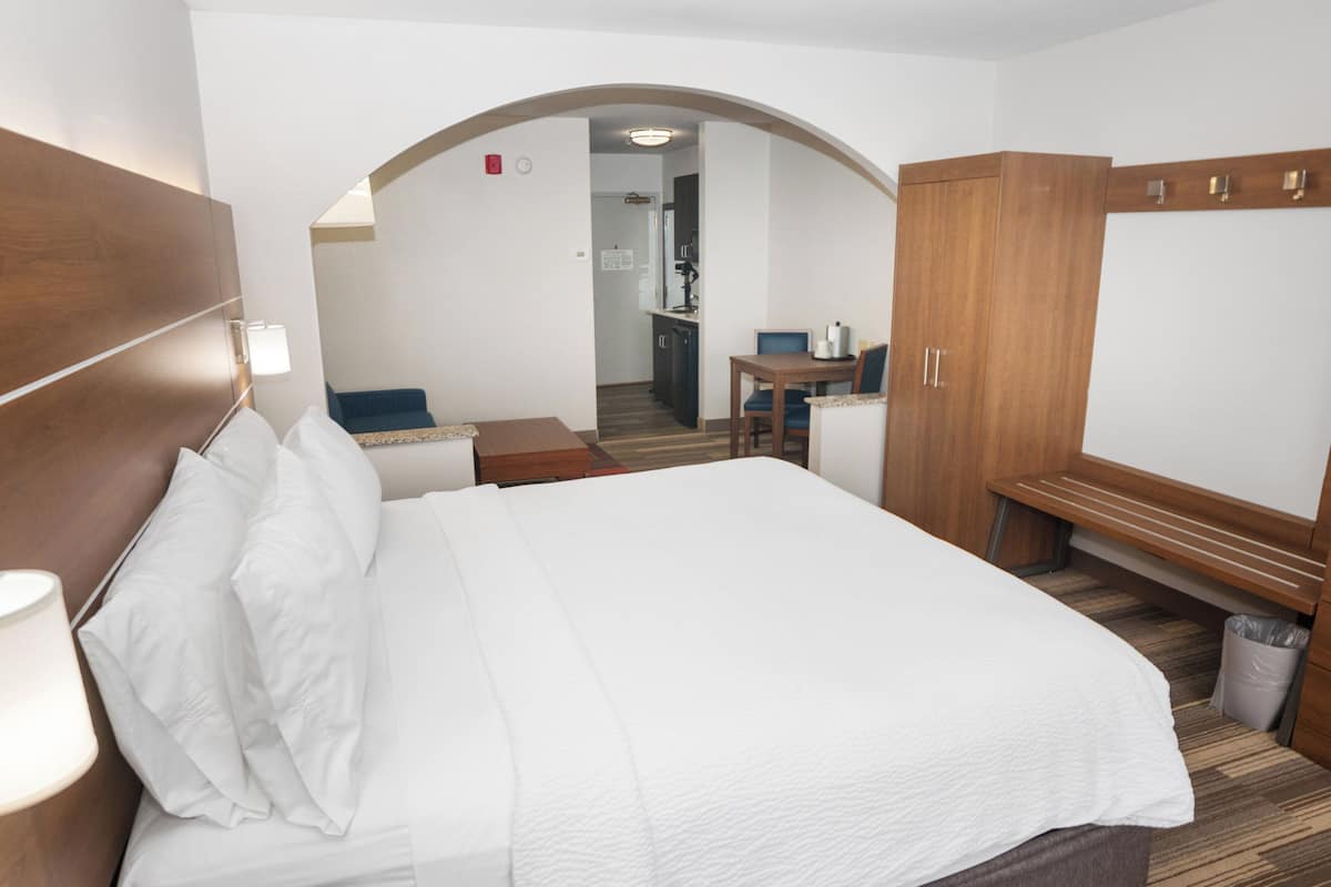 Une chambre d’hôtel avec un grand lit, une armoire en bois, un bureau avec une chaise et un petit coin salon.