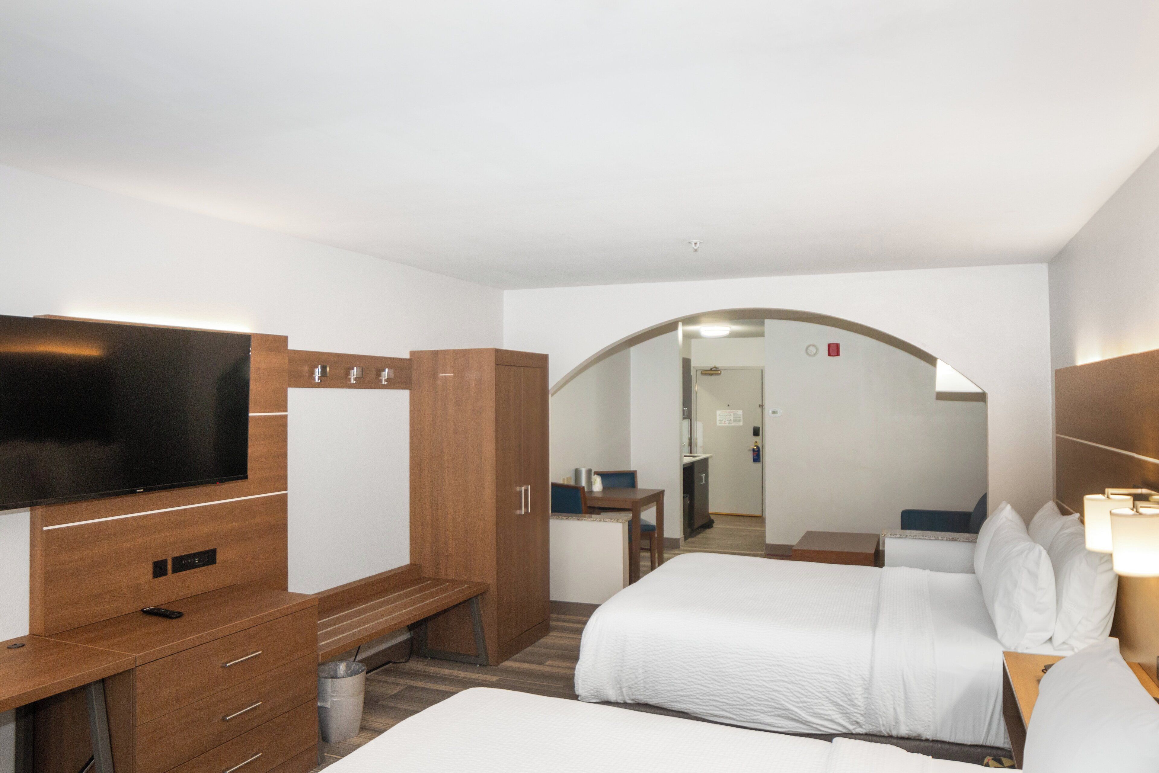 A hotel room with a TV, wooden furniture, a desk, and a bed.
