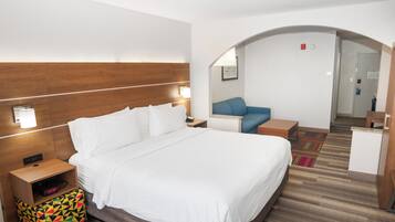 A hotel room with a large bed, bedside tables, a small desk, a colorful bag, and a mirror.