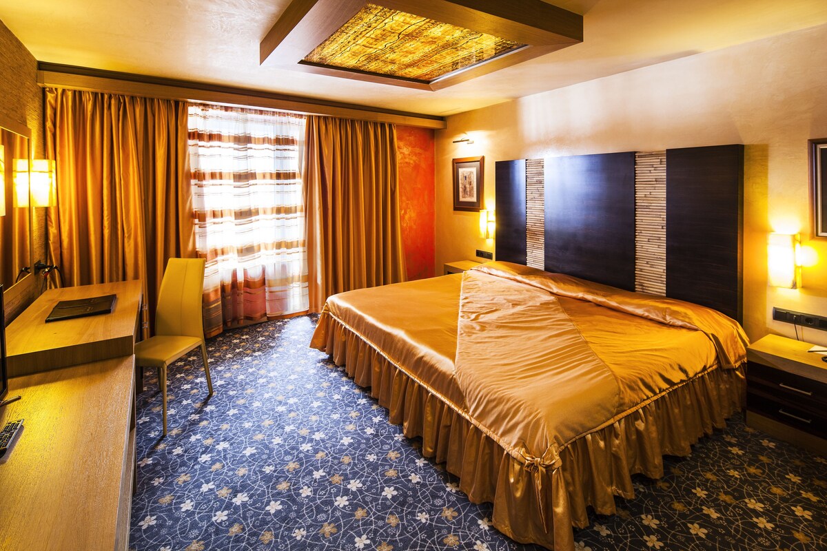 A hotel room with a large bed, a desk, a chair, and a window with curtains.