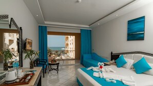 A hotel room with a bed, a desk, a chair, a table, and a view of the ocean.